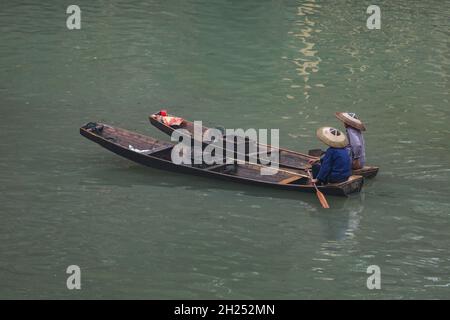 Deux hommes dans un conique traditionnel ont des échantillonages de pagaie sur la rivière Tuojiang à Fenghuang, en Chine. Banque D'Images