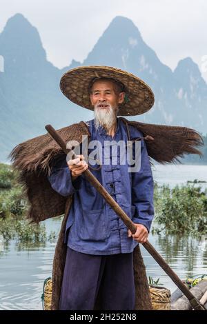 Un pêcheur cormorant au cap traditionnel sur la rivière Li.Xingping, Chine, avec des karsts de calcaire derrière. Banque D'Images