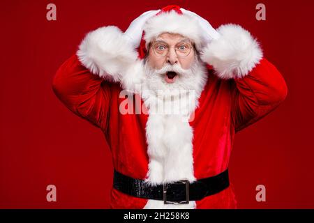 Photo de l'homme choqué impressionné retraité habillé santa claus costume ceinture bras tête ouverte bouche isolée couleur rouge arrière-plan Banque D'Images