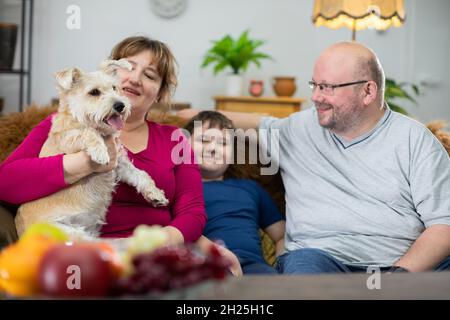 Une famille s'assoit sur un canapé et la mère tient un chien déchiqueuse dans ses bras. Banque D'Images