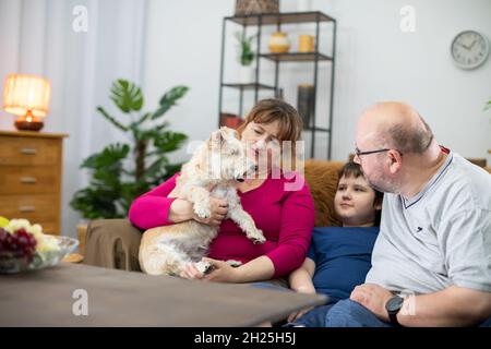 Une famille s'assoit sur un canapé et la mère tient un chien déchiqueuse dans ses bras. Banque D'Images