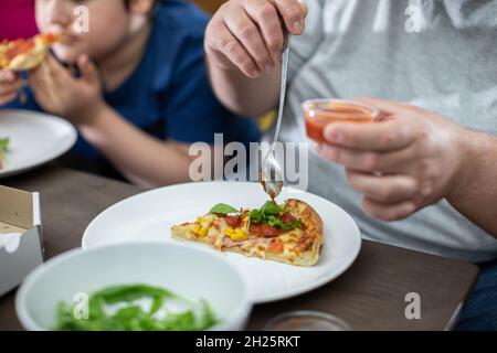 Le père met de la sauce tomate sur une tranche de pizza.Mère attend son tour. Banque D'Images