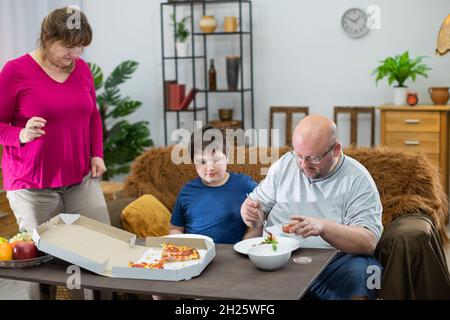 Le père met de la sauce tomate sur une tranche de pizza.Mère attend son tour. Banque D'Images