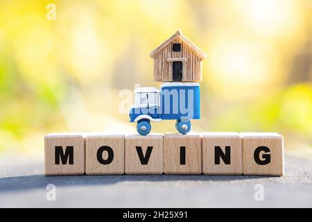 LE mot SE DÉPLACE fait de blocs de lettres en bois sur une souche d'arbre avec un camion jouet ayant une petite maison sur le dessus.Concept de service de déménagement résidentiel. Banque D'Images