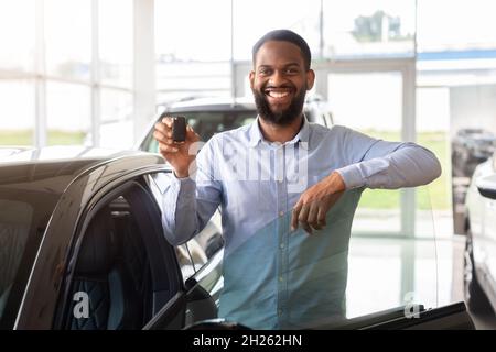 Heureux propriétaire.Homme noir gai debout près d'une nouvelle voiture et tenant les clés Banque D'Images