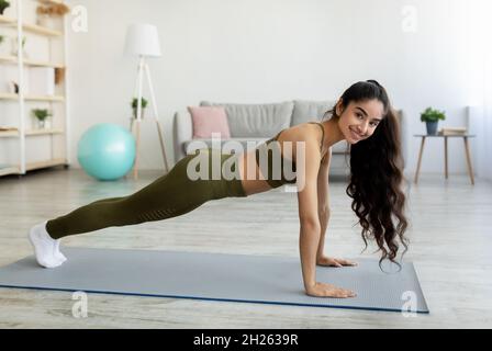 Une jeune femme indienne debout en planche pose sur un tapis de yoga à la maison, sur toute la longueur Banque D'Images