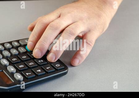 Les doigts de l'homme appuient sur les touches de la calculatrice noire.Le financier effectue des calculs mathématiques sur un appareil électronique.Intérieur.Mise au point sélective. Banque D'Images