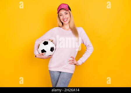 Photo portrait femme souriante en chapeau gardant le ballon de soccer isolé couleur jaune vif fond Banque D'Images