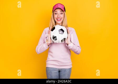 Photo portrait femme souriante en casquette garder le ballon de football rire heureux isolé couleur jaune vif fond Banque D'Images