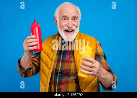 Portrait d'un joli homme joyeux aux cheveux gris tenant des bouteilles avec une sauce isolée sur fond bleu vif Banque D'Images