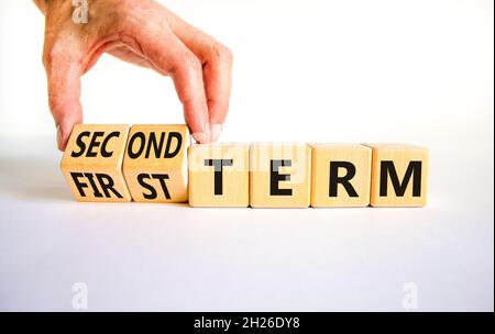 Symbole du premier ou du deuxième terme.L'homme d'affaires tourne des cubes en bois, change les mots du premier terme au deuxième terme.Belle table blanche, fond blanc.Affaires Banque D'Images
