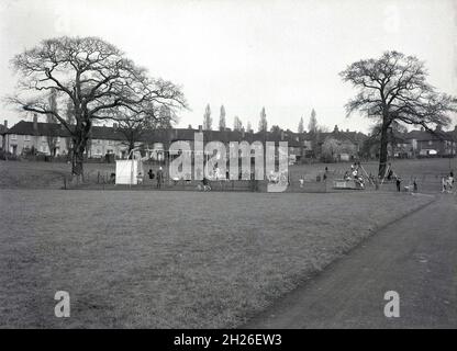 années 1950, historique, vue sur un parc public de banlieue et un terrain de jeu pour enfants, avec une terrasse de logement de conseil au loin.Sud de Londres, Angleterre, Royaume-Uni. Banque D'Images