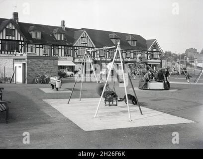 Années 1960, historique, vue sur un terrain de jeu pour enfants avec balançoires et rond-point et cheval à bascule traditionnel situé à côté d'un défilé de banlieue de tudor de magasins, sud de Londres, Angleterre, Royaume-Uni, peut-être Abbey Wood ou Eltham.Une des boutiques est une coopérative de Royal Arsenal, à l'époque une grande coopérative de consommateurs dans le sud-est de Londres. Banque D'Images