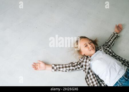 Vue en grand angle d'une petite fille souriante couchée sur le sol, étalant les bras et les jambes, faisant de l'ange. Banque D'Images