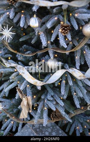 Gros plan de branche de sapin de Noël bleu avec boules décoratives et guirlandes dessus. Banque D'Images