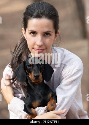 Jeune femme caucasienne embrassant le dachshund noir lisse aux cheveux miniatures dans la forêt Banque D'Images