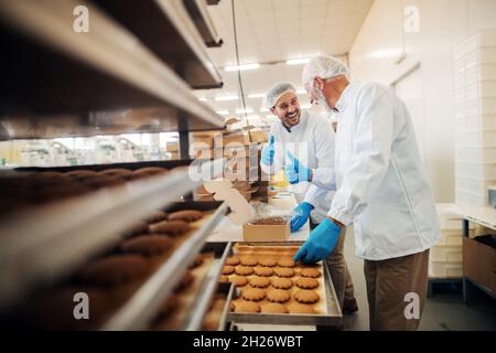 Les travailleurs emballant des biscuits dans des boîtes lorsqu'ils se trouvent dans une usine alimentaire. Banque D'Images