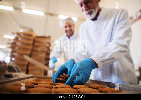 Gros plan de l'homme ramassant des biscuits tandis que l'autre emballage dans une boîte.Intérieur de l'usine alimentaire. Banque D'Images