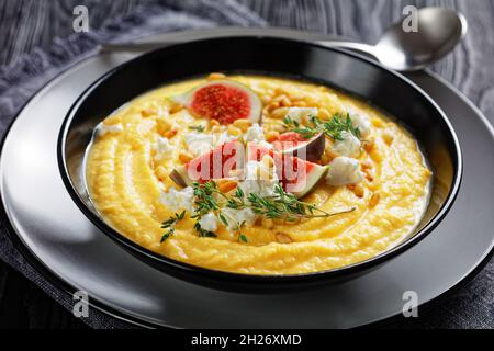 Soupe à la crème de potiron au thym servie dans un bol noir avec féta et figues servies sur un fond en bois avec une cuillère, vue du dessus, gros plan Banque D'Images