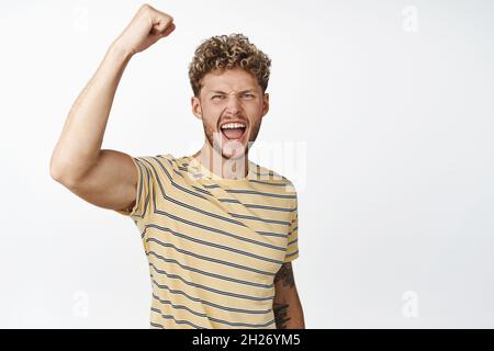 Un homme blond motivé et sympathique qui se déporte, proteste, se hante le poing fermé et crier pour vous encourager, applaudissent, se tenant sur fond blanc Banque D'Images