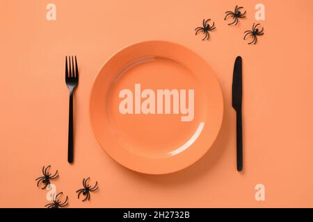 Dîner d'Halloween avec assiette orange vide décorée d'araignées noires sur fond orange.Vue de dessus.Concept alimentaire.Table amusante. Banque D'Images