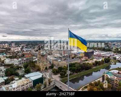 Drapeau jaune et bleu de l'Ukraine qui agite dans le vent sur le mât avec un paysage de nuages lourds épiques, vue aérienne de la ville sur le remblai de la rivière d'automne Lopanan, Holy Annunci Banque D'Images