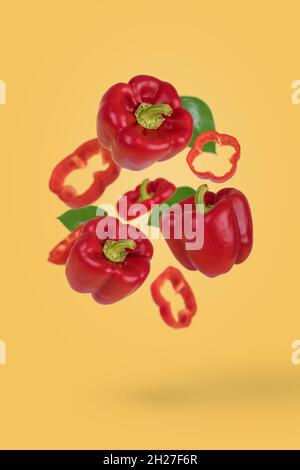 Concept créatif d'aliments ou de légumes.Poivrons rouges entiers et coupés en tranches frais volant dans l'air isolé sur fond jaune pastel.Alimentation saine, alimentation, v Banque D'Images