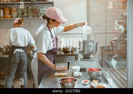 Femme verse de la farine de blé dans un récipient sur balance numérique avec un collègue de boulangerie Banque D'Images