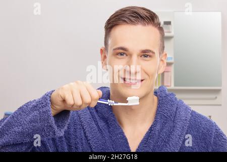 Jeune homme dans un peignoir se brossant les dents devant un miroir dans une salle de bains Banque D'Images