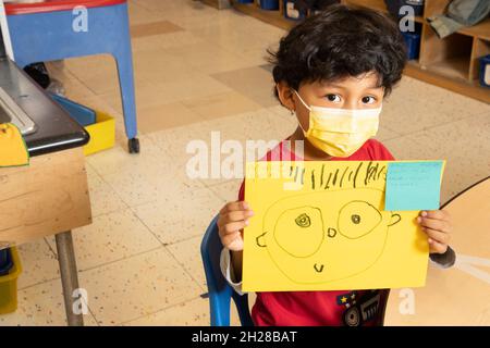 Éducation préscolaire garçon de 4-5 ans tenant le dessin qu'il a fait de la personne, portant un masque facial pour protéger contre l'infection Covid-19 Banque D'Images