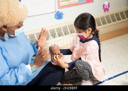 Éducation préscolaire 4-5 ans jeune fille avec poupée jouer et interagir avec le professeur, les deux portant des masques pour protéger contre Covid-19 Banque D'Images