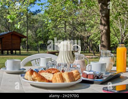 PETIT DÉJEUNER ARGENTIN DANS LE JARDIN EN VACANCES.BISCUITS, CROISSANTS, JUS D'ORANGE, LAIT, CAFÉ.HORIZONTALE.ARRIÈRE-PLAN FLOU Banque D'Images