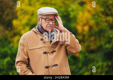 Portrait extérieur d'un homme âgé inquiet en manteau d'hiver.Il a mal à la tête. Banque D'Images