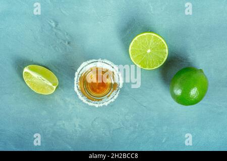 Tequila Gold shot avec des limes, liqueur mexicaine avec un bord salé, tiré du dessus sur un fond bleu avec un lieu pour le texte Banque D'Images