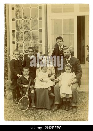 Photographie Edwardienne originale d'une grande famille attrayante, 6 enfants, principalement des garçons, assis à l'extérieur d'une grande maison. La mère a un bébé ou un tout-petit sur ses genoux qui est vêtu de vêtements de fille mais qui pourrait être un garçon car les jeunes enfants étaient habillés de la même façon à ce moment-là. Riches riches et riches pour faire de la famille. Royaume-Uni vers 1908, Royaume-Uni Banque D'Images