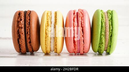 Bannière. Quatre macarons colorés verts, roses, jaunes et bruns sur fond rustique en bois blanc. Macarons de petits gâteaux français doux et colorés. Banque D'Images