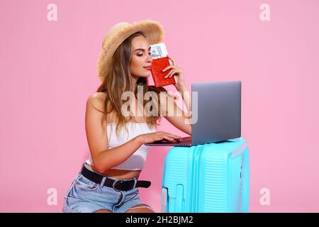 Une fille voyageur tient un passeport, des billets, de l'argent avec des valises tout en utilisant un ordinateur portable.Concept de voyage Banque D'Images