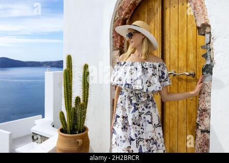 Bonne jeune femme en robe élégante et chapeau sur les rues de l'île de Santorini le jour d'été ensoleillé Banque D'Images