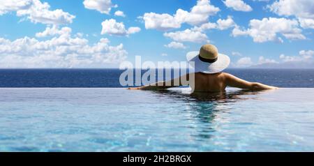 femme avec chapeau de paille dans la piscine à débordement avec vue sur la mer dans un complexe de luxe. vacances d'été. espace copie Banque D'Images