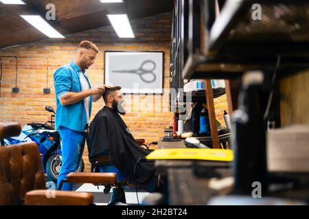 Un coiffeur de sexe masculin coupe les cheveux d'un client dans son salon Banque D'Images