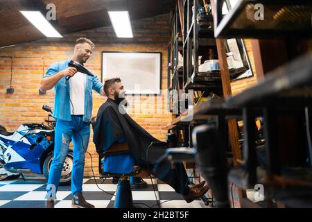 Coiffeur masculin séchant les cheveux de ses clients Banque D'Images
