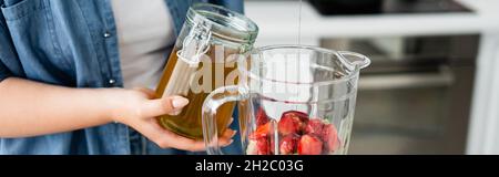 Vue rognée d'une femme de taille plus versant du miel dans un mélangeur avec des fraises, bannière Banque D'Images
