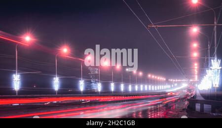 Traces de phares des voitures se déplaçant la nuit d'hiver sur le pont, illuminés par des lanternes.Lumières réfléchissantes dans l'asphalte humide. Banque D'Images