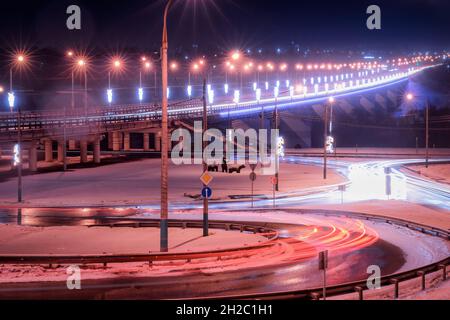 Traces de phares des voitures se déplaçant la nuit d'hiver sur le pont, illuminés par des lanternes.Lumières réfléchissantes dans l'asphalte humide. Banque D'Images