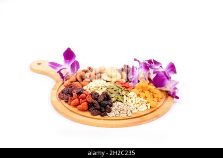 Groupe de différents types de fruits secs et de grains séchés avec belle orchidée sur une plaque en bois isolée sur fond blanc. Banque D'Images