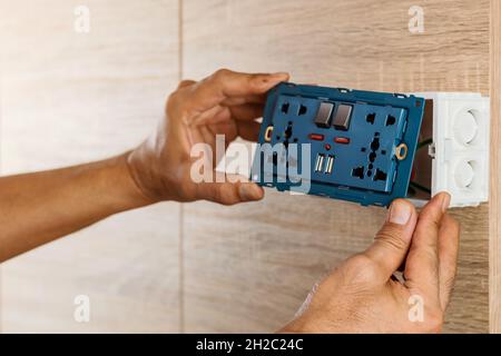 La main d'un électricien est d'installer la prise d'alimentation CA de la prise murale universelle avec port USB et on-off dans une boîte en plastique sur un mur en bois. Banque D'Images