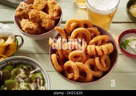 Gros plan de bols de rondelles d'oignon, ailes de poulet frites, salade et deux bouteilles de bière Banque D'Images