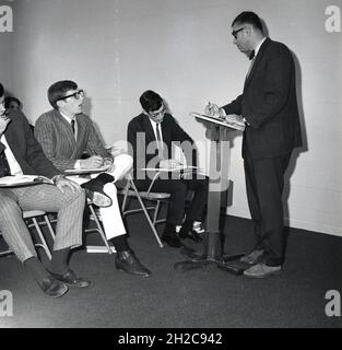 Années 1960, historique, dans une pièce quelques étudiants de premier cycle de sexe masculin assis sur des chaises en métal à l'écoute d'un professeur debout dans un lectern, donnant un discours dans un cours de philosophie, Monroe College, États-Unis Banque D'Images