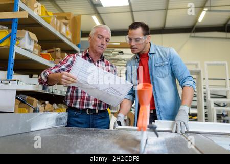 portrait de deux ouvriers discutant des plans de projet en atelier Banque D'Images