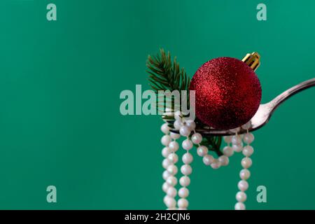 Gros plan des décorations de Noël sur une fourchette de perles blanches, une branche d'un sapin de Noël et une boule de Noël rouge sur un fond vert. Concept de nourriture festive pour noël ou nouvel an. Espace copie Banque D'Images